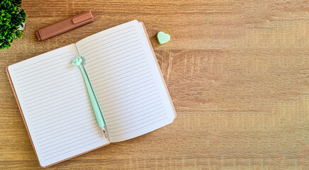 There is an open notebook with a pen and erasers on the wooden surface of the table.