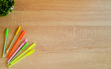 Colored pens lie on a wooden table. A flower is in the background.