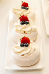 Delicious mini pavlovas topped with whipped cream, strawberries, and blueberries, arranged elegantly on a white plate.