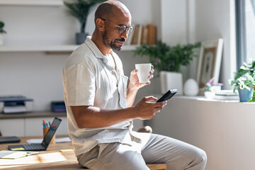 Trader working from home, drinking coffee and using smartphone indoors