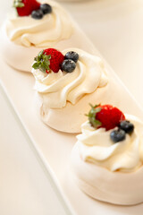 Delicious pavlova desserts topped with fresh strawberries and blueberries, artfully arranged on a white platter.