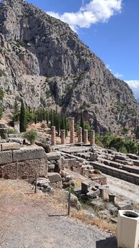 Ancient stone columns and ruins of the Temple of Apollo at Delphi, Greece. Historic archaeological, Mount Parnassus, surrounded by rocky cliffs and cypress trees. famous for the Oracle of Delphi.