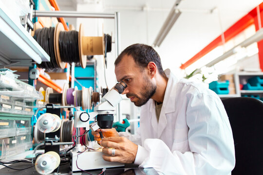 Lab technician inspecting microchip with magnifier in electronics workshop
