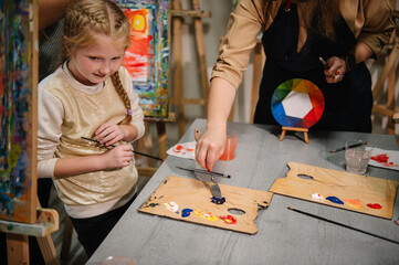 Teacher learn children to draw pictures in an art lesson. Artist explains how to mix and combine colors. Childs painting in workshop. Kids drawing brush on easel. Education, learning concept.