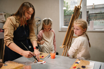 School children drawing brush landscapes on easel. Education, creativity and learning concept. Teacher explains to girls how to draw pictures in art class. Childs enjoy painting in workshop