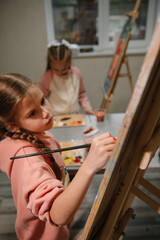 Group of school children drawing with brush landscapes on easel. Childs enjoy painting in workshop. Art lesson. Kids draw pictures in art class. Education and learning concept. Mix and combine colors.