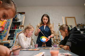 Artist explains how to mix and combine colors. Teacher learn children to draw pictures in an art lesson. Childs painting in workshop. Kids drawing brush on easel. Education, learning concept.