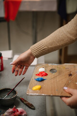 Girl mixing and combining colors. Woman painting in a workshop. Female is drawing a picture in art class. Art lesson. Education and learning concept. Hands drawing with brush on easel. Closeup.