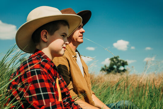 Father and son wearing cowboy hats sitting together on grass outdoors