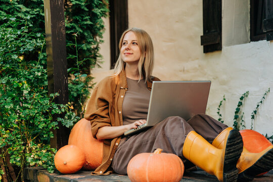 Person working with laptop on porch with pumpkins in autumn