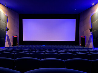 Empty cinema hall with blue lighting and blank screen before movie premiere and copy space concept