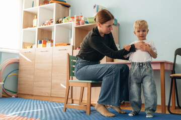 Woman is sitting and checking the boy. Preschool child with teacher during developmental activities...