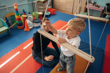 Holding by the wooden stick on surface that is swinging. Preschool child with teacher during...