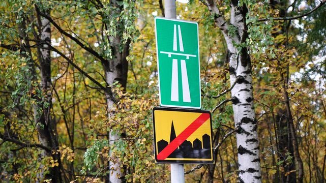 Roadside signs at forest road showing end of town and beginning of highway, surrounded by autumn trees, symbolizing transition from urban environment to open countryside drive