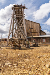 Olav's Mine: A wooden mining building rises prominently in the rural area of R&oslash;ros, Norway, surrounded by weathered buildings and rocky terrain, capturing the essence of a bygone mining era.