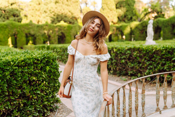 Obraz premium Young woman in a summer dress enjoying the sunshine in a beautiful garden setting during the late afternoon
