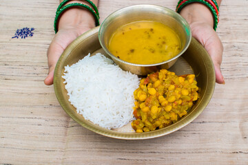 lady hand serving thali or plate with steamed rice (chawal), dal, and lauki ki sabji (bottle gourd curry) to devotees observing the Nahay Khaye ritual, the first day of Chhath Puja. Holy food