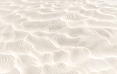 Obraz premium Close-up of fine white sand forming gentle waves and soft light shadows. Natural beach texture ideal for backgrounds, travel, summer, and vacation concepts in clean minimalist design.