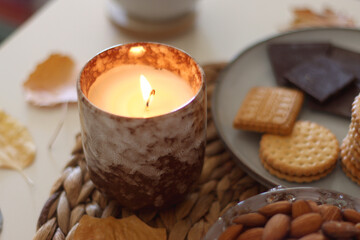 Lit candles, cookies, chocolate, nuts, tea, wine, pumpkins, books, reading glasses and autumn leaves on the table. Autumnal hygge at home. Selective focus.