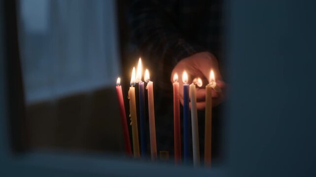 Cropped close up shot of hands of unrecognizable person lighting up candles on hanukkiah with burning shammash on final day of Hanukkah celebration