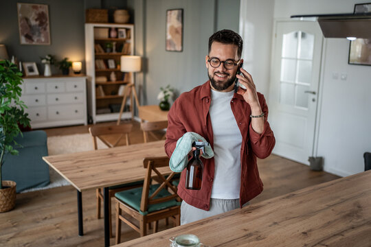 Man cleaning home while talking on phone - Powered by Adobe