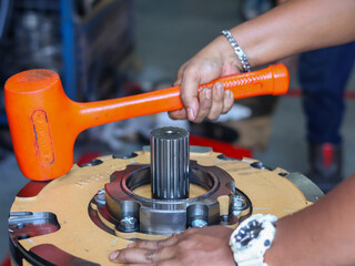 A worker's hands using a striking orange mallet to adjust a precision metal spline on heavy machinery, showing industrial assembly.