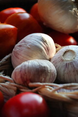 Garlic bulbs stored in a small woven wooden basket with tomatoes, rustic kitchen and organic food concept