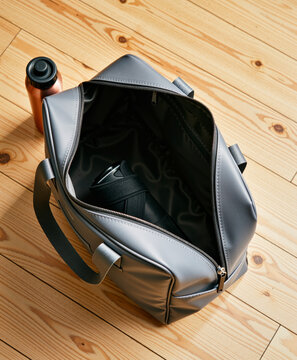Open grey gym bag with water bottle on a light wooden floor