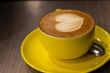 A vibrant yellow cup of latte art featuring a perfectly formed heart, resting on a matching saucer on a sleek table, inviting warmth and comfort.