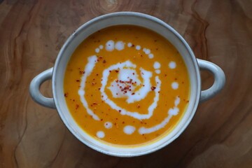 Autumnal pumpkin soup served with cream and chili flakes in a small pot, perfect food photography, cozy seasonal meal concept for thanksgiving