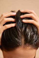 Naklejka premium Close-up of woman’s hands applying hair oil to scalp, showing shiny texture and healthy roots, soft diffused light, clean beige background.