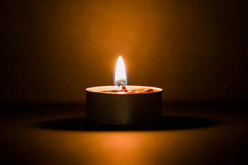 Small burning candle in small container on dark black background. Closeup. Front view.