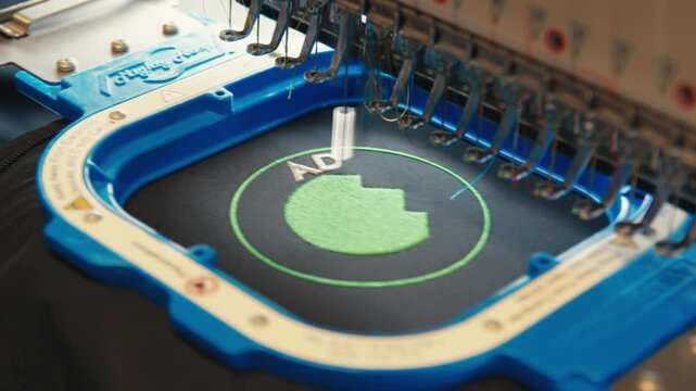 Automated embroidery machine sews precise green and white logo onto garment.