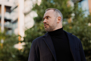 Elegant man in turtleneck and coat looking away on city street