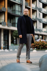 Full length of elegant man in coat looking at camera on city street © Dmytro Hai