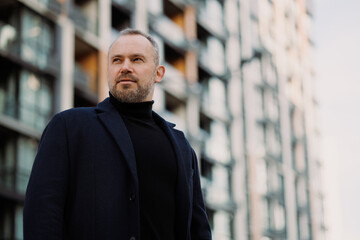 Fototapeta premium Portrait of elegant businessman in coat standing on city street