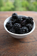 Front close-up of fresh wild blackberries in a white bowl on rustic wood. Focus on texture, superfoods, natural light, and shallow depth of field.