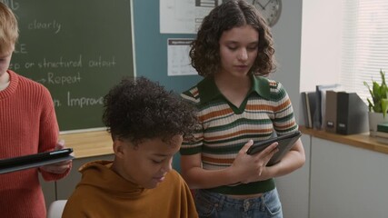 Medium close-up of enthusiastic African American boy writing computer code on laptop at programming lesson, Caucasian girl pointing and helping with advice, student working on tablet in background - Powered by Adobe