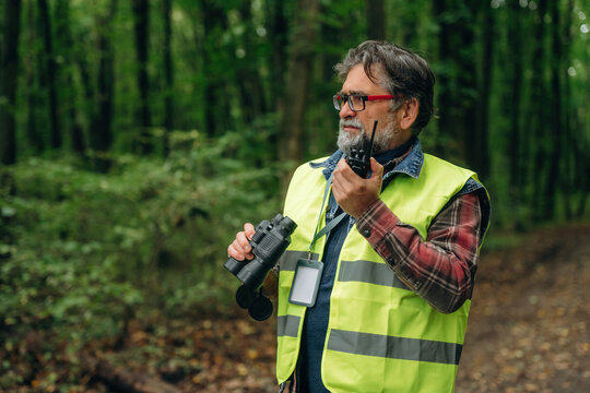 Radio walkie talkie and binoculars in hands. Senior forest ecologist is working in the woods. In the uniform