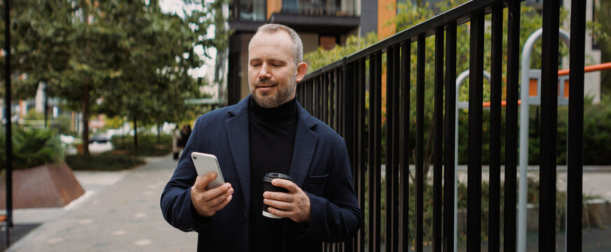 Banner of businessman using smartphone and holding coffee to go on street in autumn