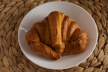 Croissant on a white plate, on a small esparto tablecloth.