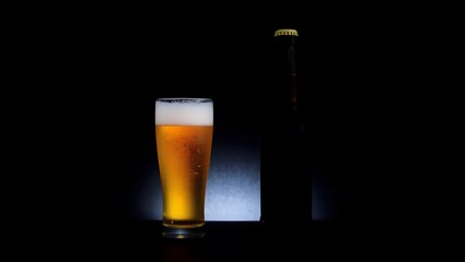A glass of cold golden lager with foam and froth is isolated on a dark background