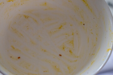 White ceramic bowl with visible yellowish food stains and crumbs left after eating, photographed in natural light from above.