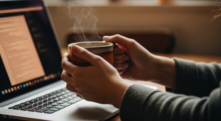 Fototapeta premium Cozy Home Office: Hands Holding Steaming Coffee Mug with Laptop