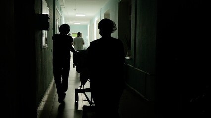 Two medical professionals pushing a gurney down a dimly lit hospital corridor, navigating swiftly after a surgical procedure, embodying urgency and teamwork in critical care