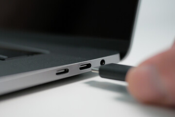 Hand plugging in a USB Type C cable into a port on a modern notebook or laptop computer. Close up.
