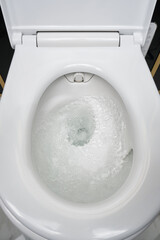 White ceramic toilet bowl in the process of washing it off. Close up swirling, flushing water in toilet bowl. Selective focus.