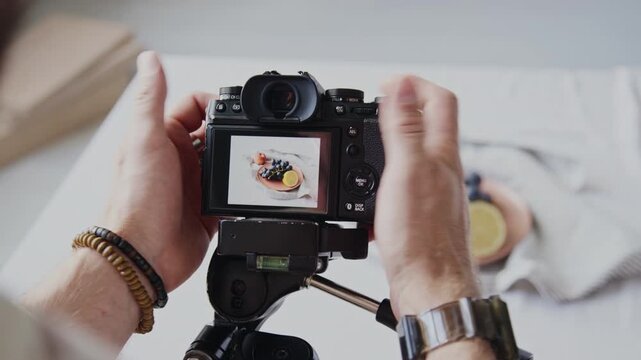 Unrecognizable male hands pushing buttons to take photo of fresh and juicy fruits on beige plate placed on table