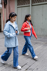 Two young girls walking down a street wearing blue and red jackets