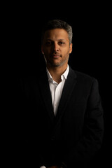 A man in a suit and white shirt is standing in front of a black background